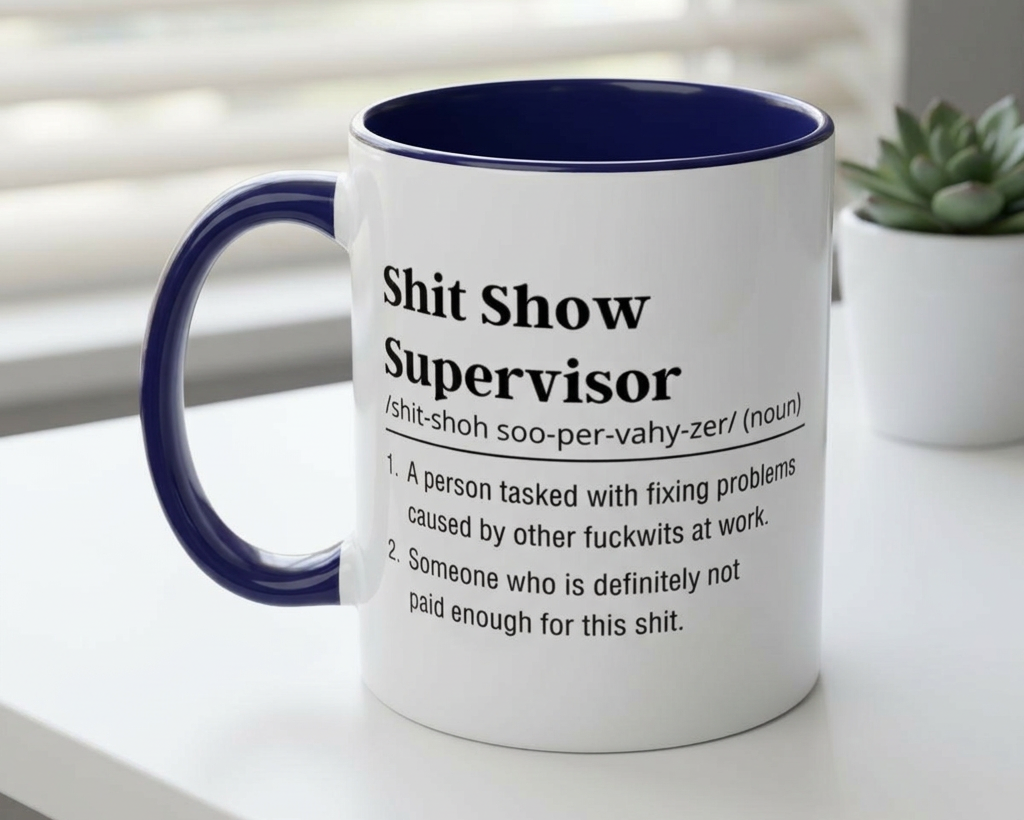 Mug with definition of 'Shit Show Supervisor' on a white surface with a plant in the background