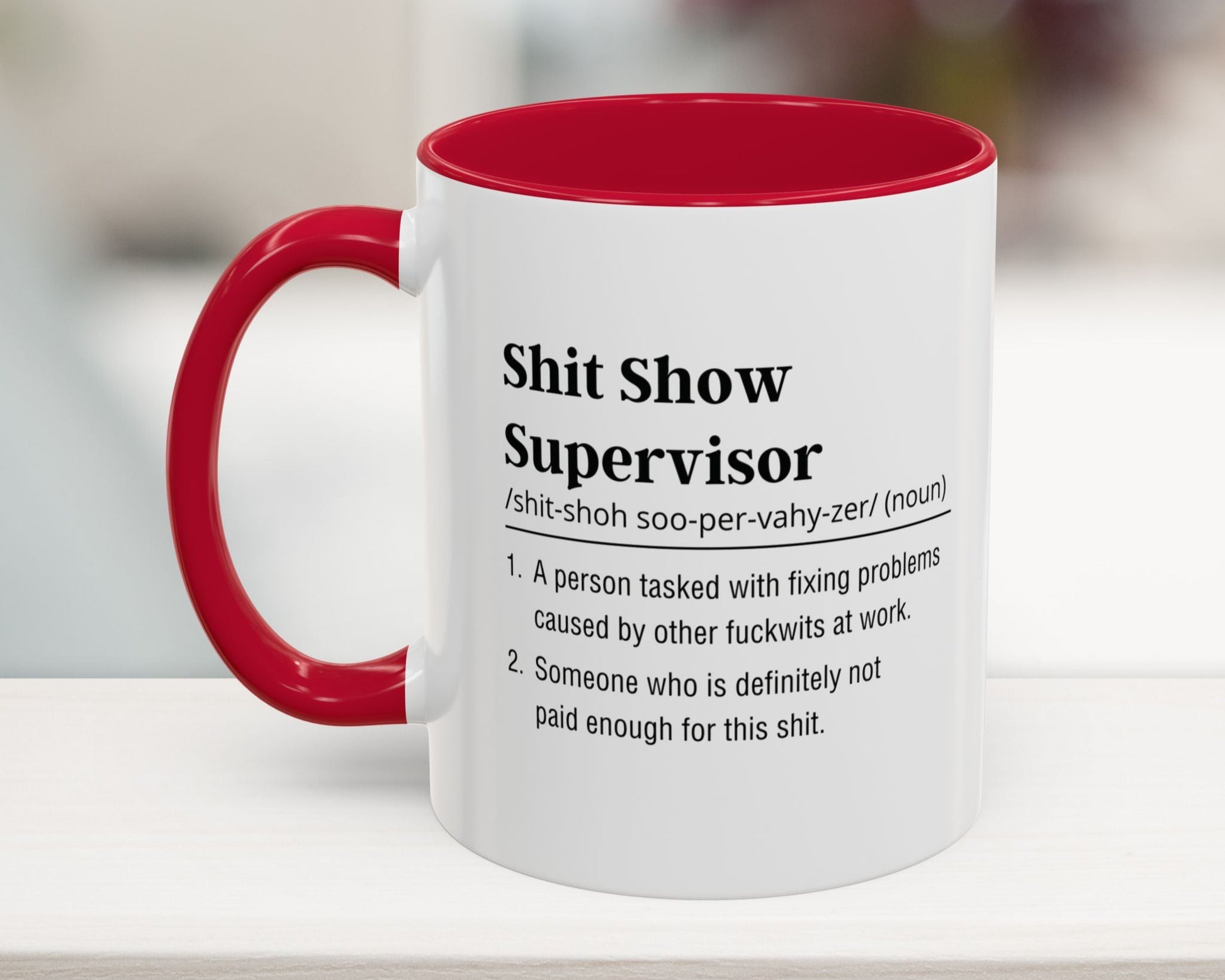 White mug with red interior and handle featuring humorous definition text on a blurred background