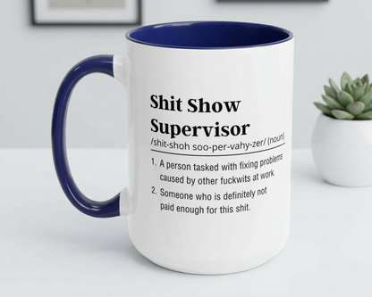 Mug with text definition of 'Shit Show Supervisor' on a white surface with a plant in the background