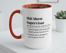 White mug with red handle featuring text on a white surface with a plant in the background