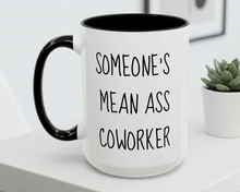 White mug with black interior and handle, featuring text, on a white surface with a plant in the background.