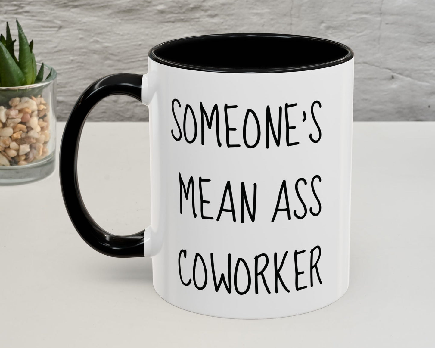 Mug with text 'SOMEONE'S MEAN ASS COWORKER' on a neutral background