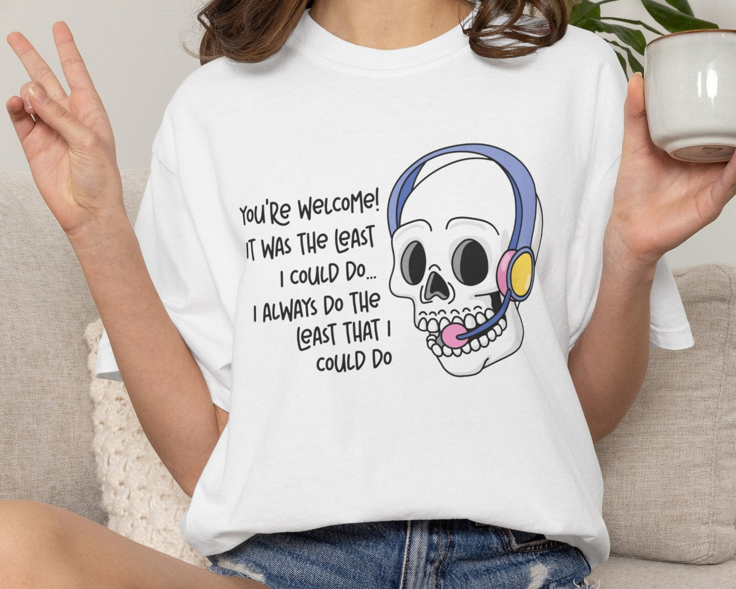 Person wearing a white t-shirt with a skull graphic and text, holding a mug.