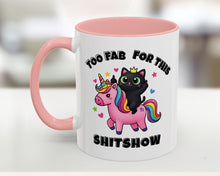 Mug with a black cat on a unicorn, pink handle, and text 'Too Fab for this Shitshow' on a blurred background.