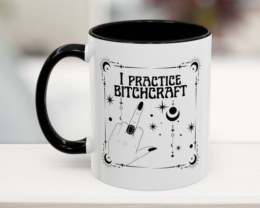 Mug with 'I Practice Bitchcraft' text and black handle on a white surface.